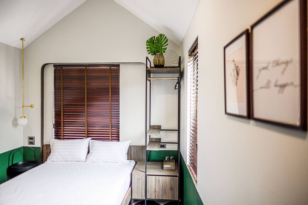 Een slaapkamer met een bed, een groen nachtkastje, een wandplank met een plant en een gekaderd citaat aan de muur.