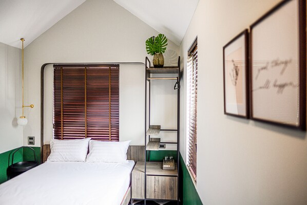 Une chambre à coucher avec un lit, une table de chevet verte, une étagère fixée au mur avec une plante, et une citation encadrée accrochée au mur.