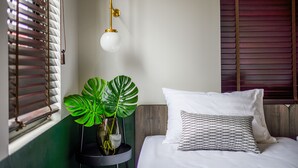 A neatly made bed with white and patterned pillows, a bedside plant, and a hanging light fixture.