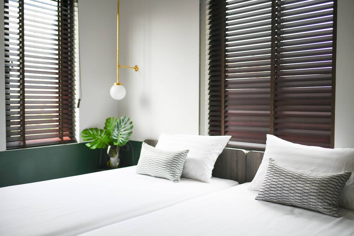 Een slaapkamer met een bed, twee kussens, een hanglamp en een plant.