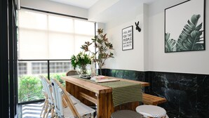A dining area with a wooden table, four chairs, a vase with flowers, and two framed pictures on the wall.