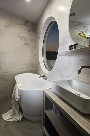 A modern bathroom with a freestanding bathtub, a rectangular sink, and a large oval mirror. - Acropolis Junior Suite (Athens)