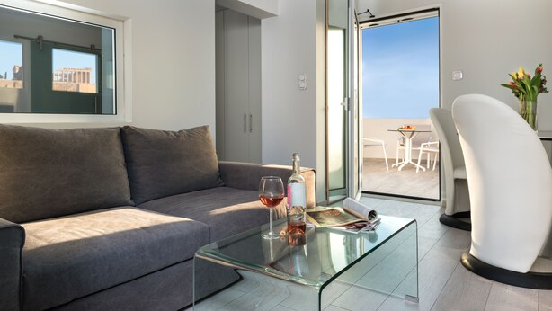 A modern living room with a glass coffee table, a grey sofa, and a view of the outside balcony.