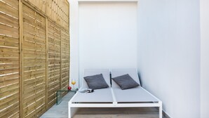 A small, white, single-bed room with a wooden slatted wall, a glass table with a magazine, and a glass of orange juice.
