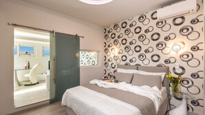 A modern bedroom with a bed, a glass table with a vase, and a patterned wall.