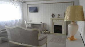 A room with a white desk, a fireplace, a television mounted on the wall, and a decorative lamp. - Hotel Vetraz (Vitebsk)