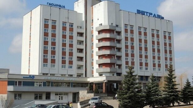 A multi-story hotel with a central atrium, a parking area, and a sign indicating a business center. - Hotel Vetraz (Vitebsk)