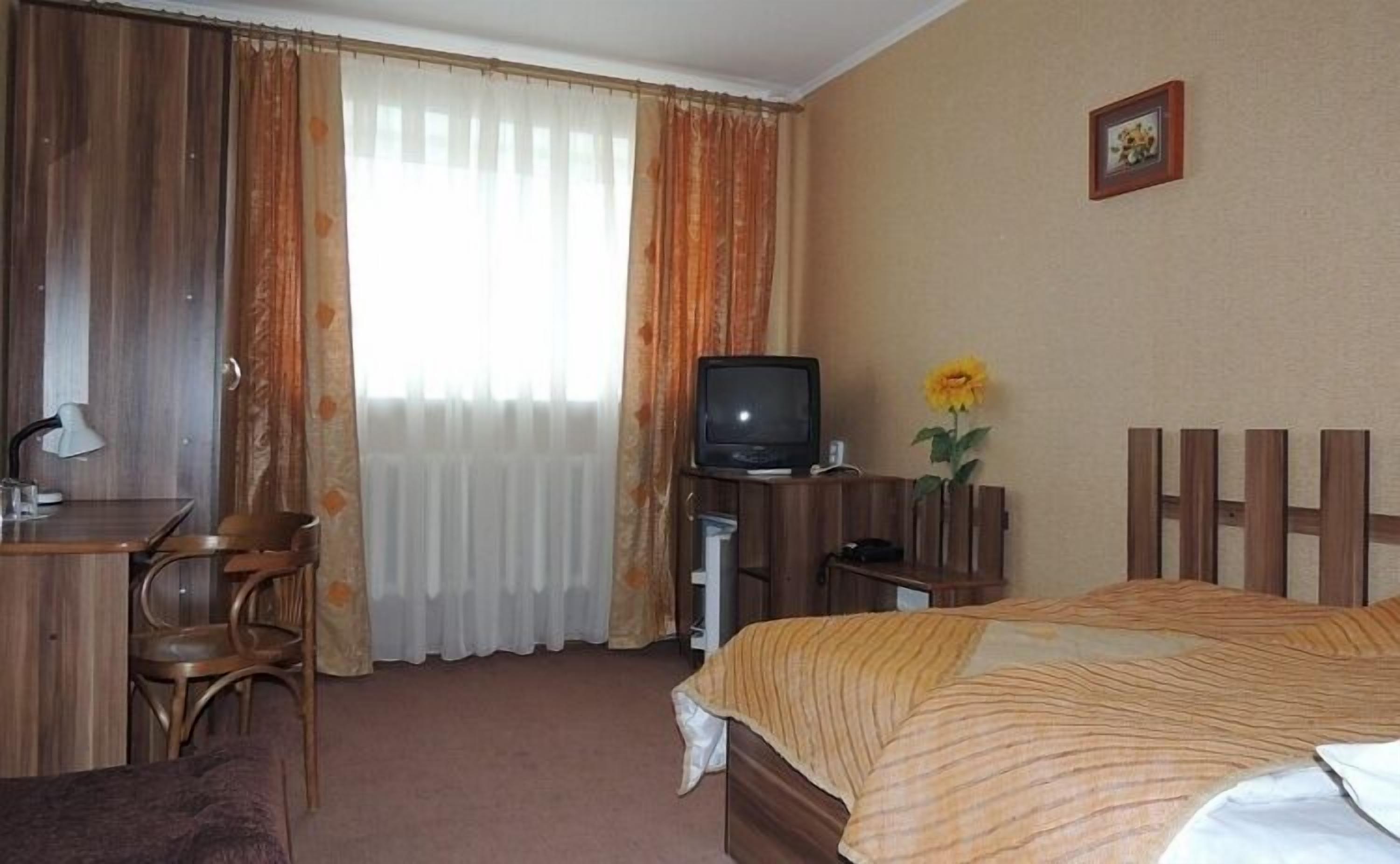 Habitación de hotel con una cama, un escritorio con lámpara, televisor y un cuadro en la pared.