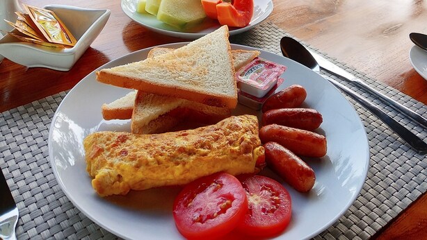 A breakfast setting with a plate of toast, sausages, tomatoes, and a small bowl of jam. - The Tetamian Bali (Sukawati)