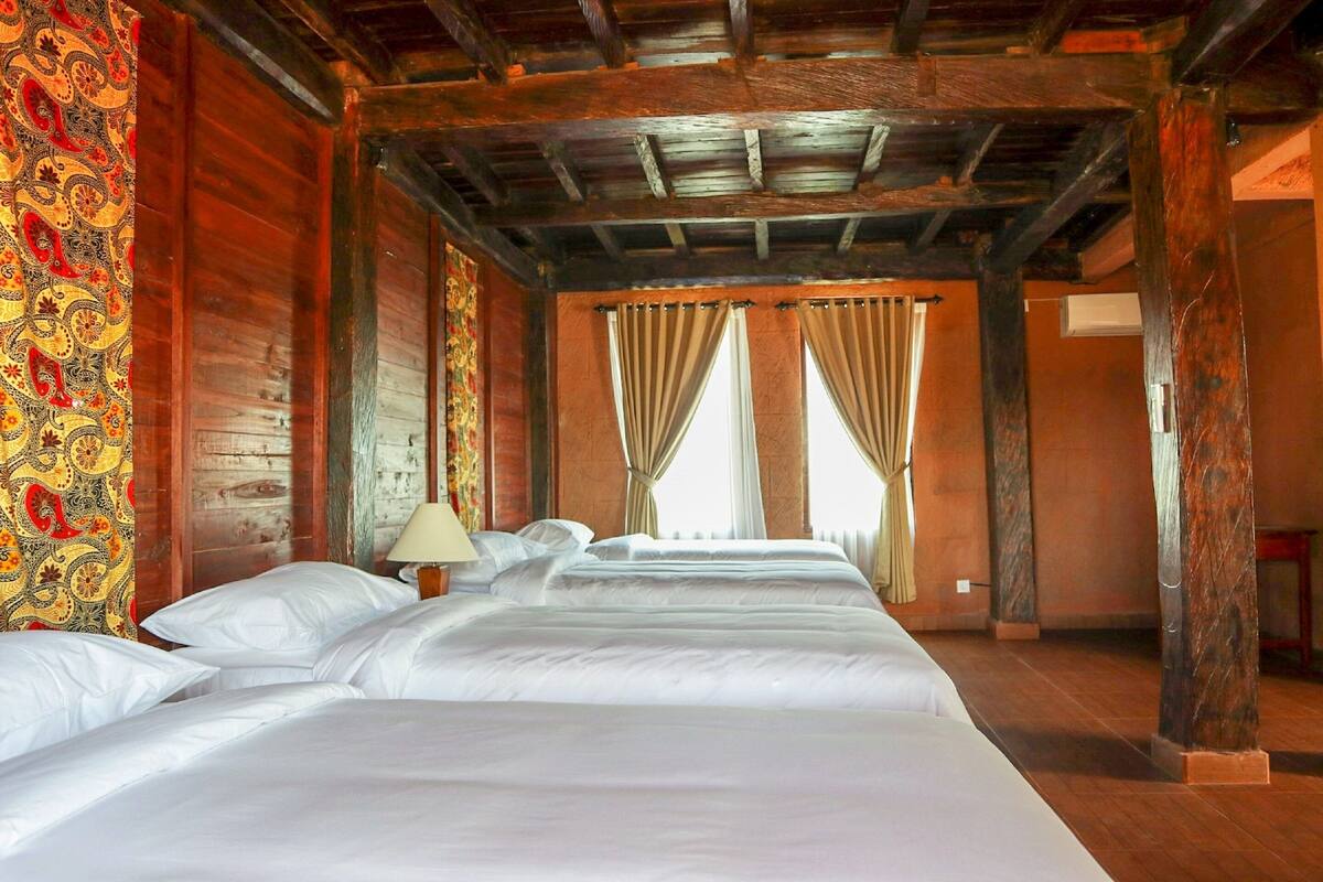 Ein Hotelzimmer mit Holzboden, einem großen Bett mit weißen Laken und einem Fenster mit Vorhängen.