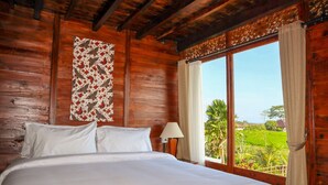 A wooden room with a bed, a window with curtains, and a wall hanging. - The Tetamian Bali (Sukawati)