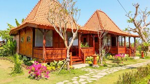A traditional wooden house with a tiled roof, surrounded by lush greenery and flowering plants. - The Tetamian Bali (Sukawati)