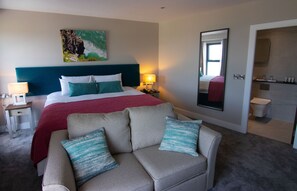 Une chambre d’hôtel comprenant un lit, un canapé, une table de chevet, une lampe, un tableau, un miroir et une salle de bain.