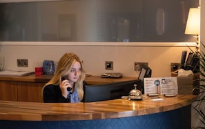 Un comptoir d’accueil d’hôtel avec un comptoir en bois, un téléphone, un écran numérique et un panneau indiquant que le Wi-Fi est gratuit.