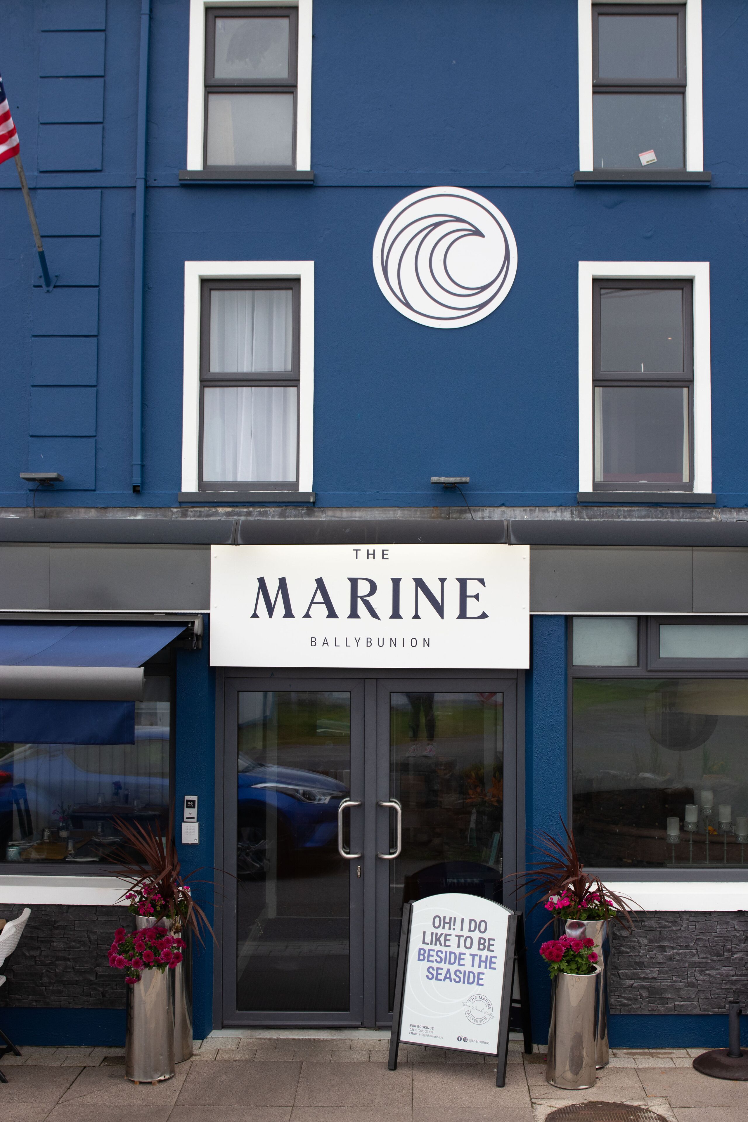 A building with a sign reading "The Marine Ballybunion" and a sign outside stating "OH! I DO LIKE TO BE BESIDE THE SEASIDE."