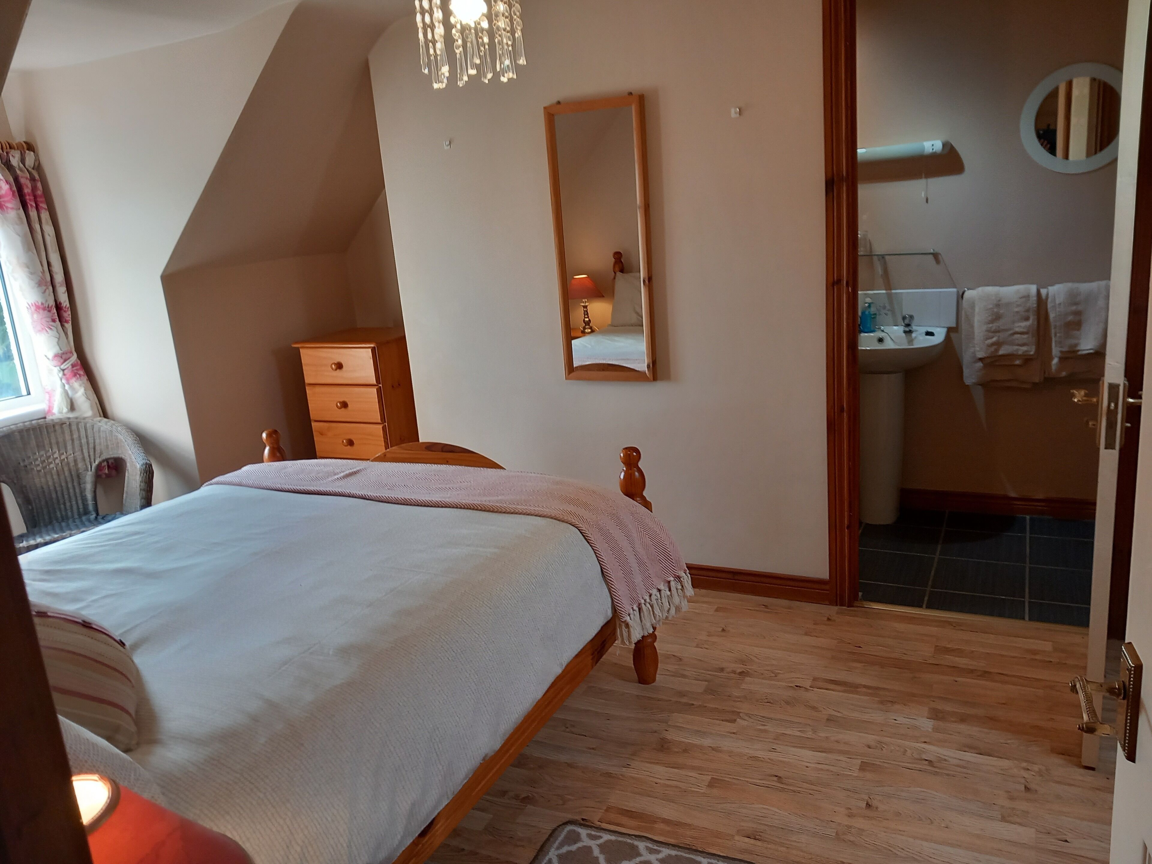 A bedroom with a bed, wooden dresser, and a bathroom visible through an open door.