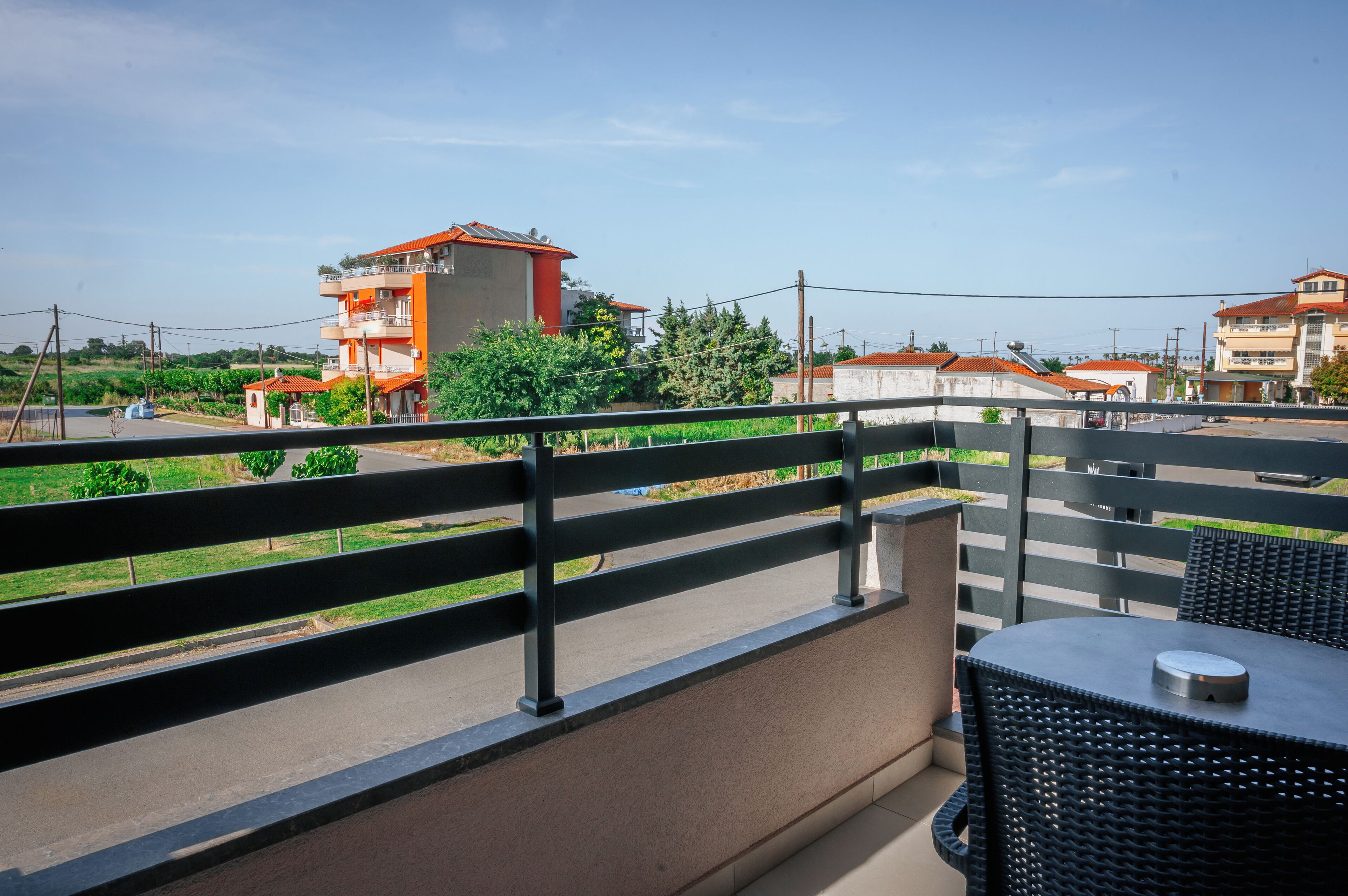 Un balcon avec une table et des chaises, donnant sur une route et des bâtiments aux toits rouges.
