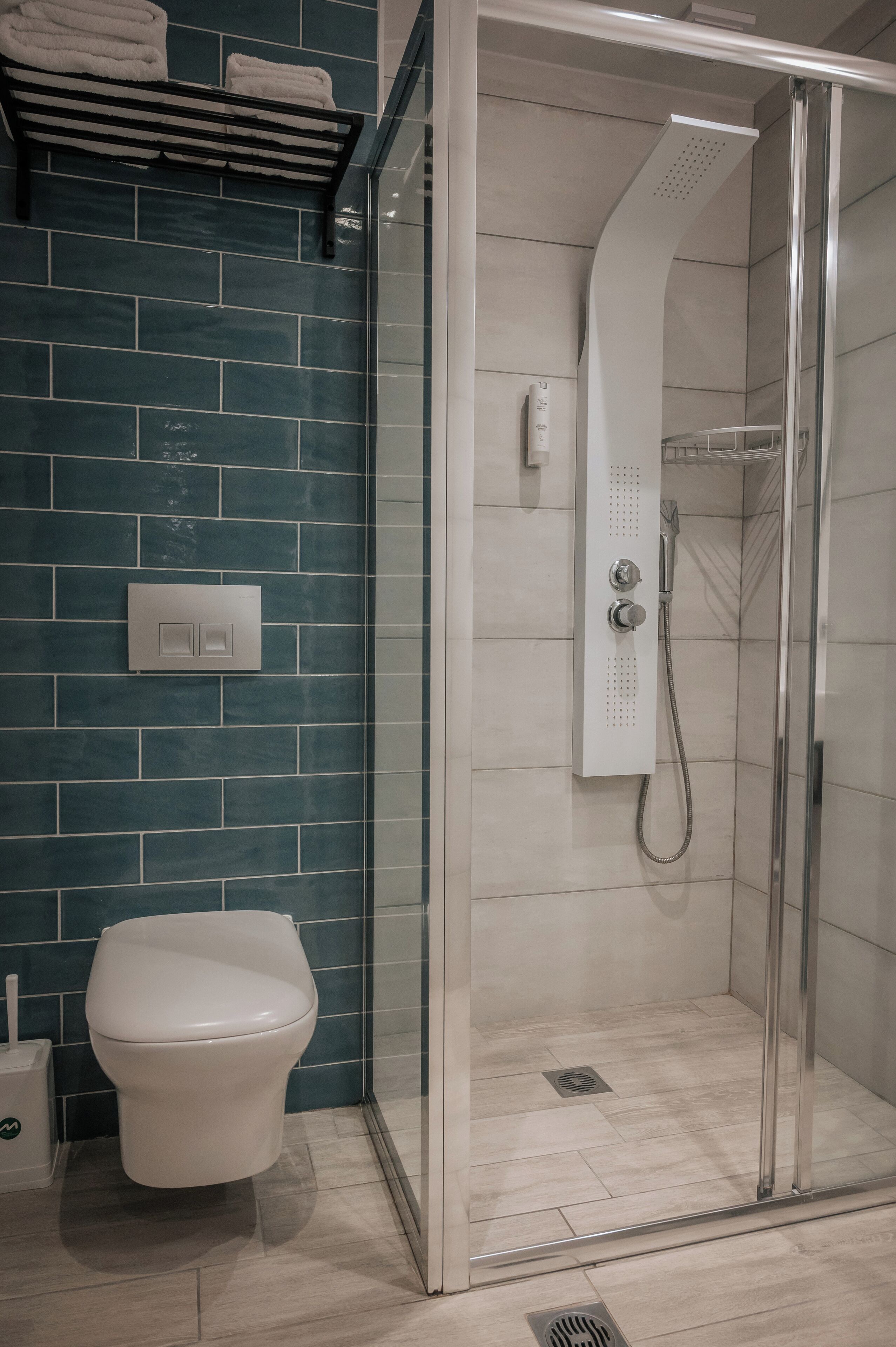 Een moderne badkamer met een douchecabine van glas, een wit toilet en een handdoekrek met opgevouwen handdoeken.