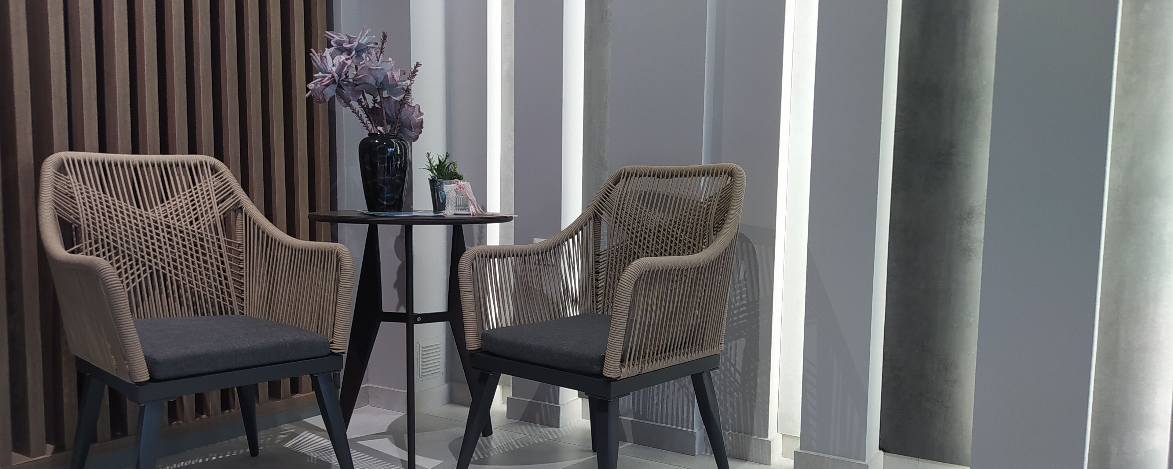 Two wicker chairs with dark cushions, a small round table, and a vase with flowers.