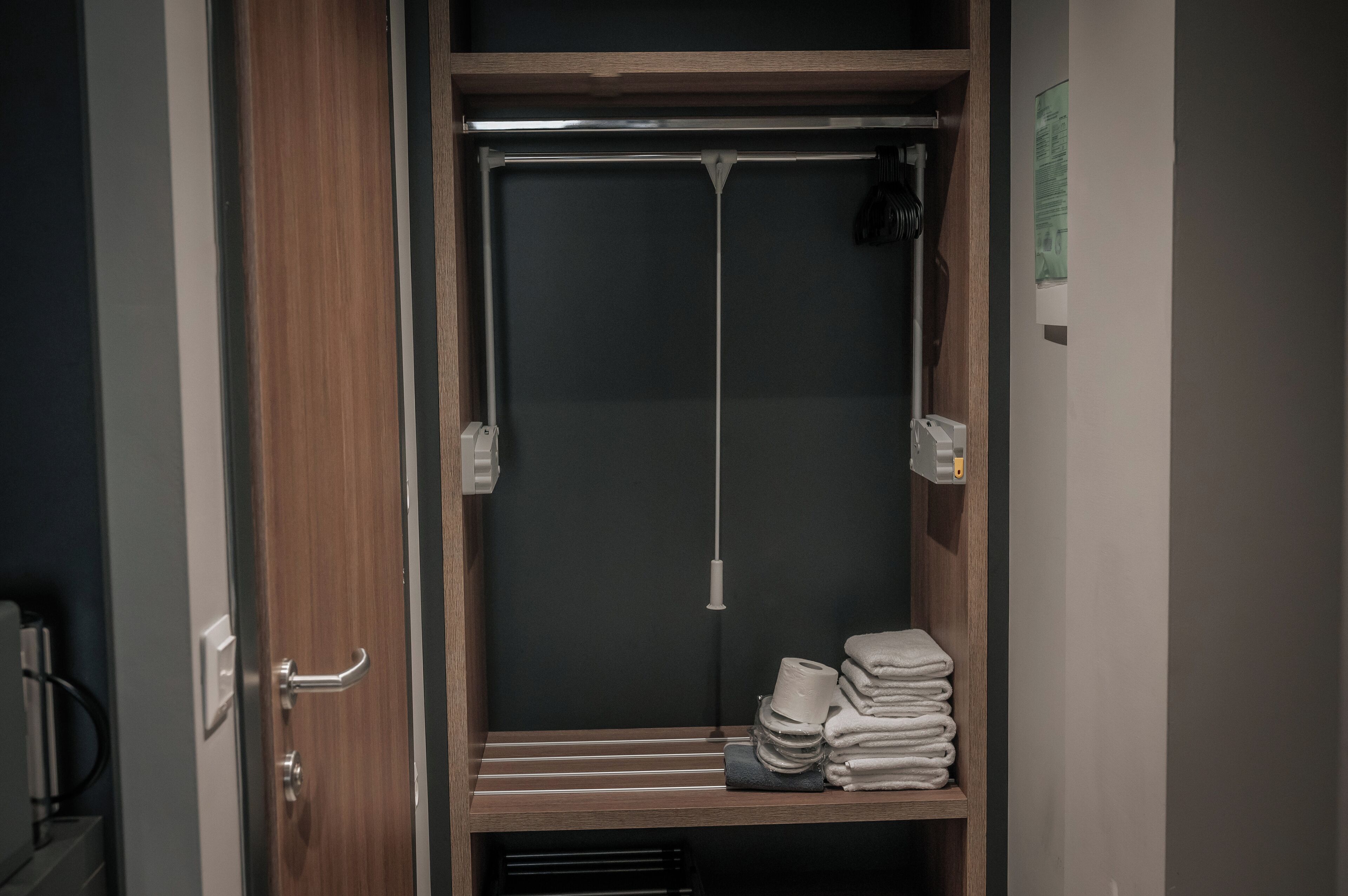Un armario espacioso con puerta de madera, una estantería de metal y toallas dobladas con cuidado.