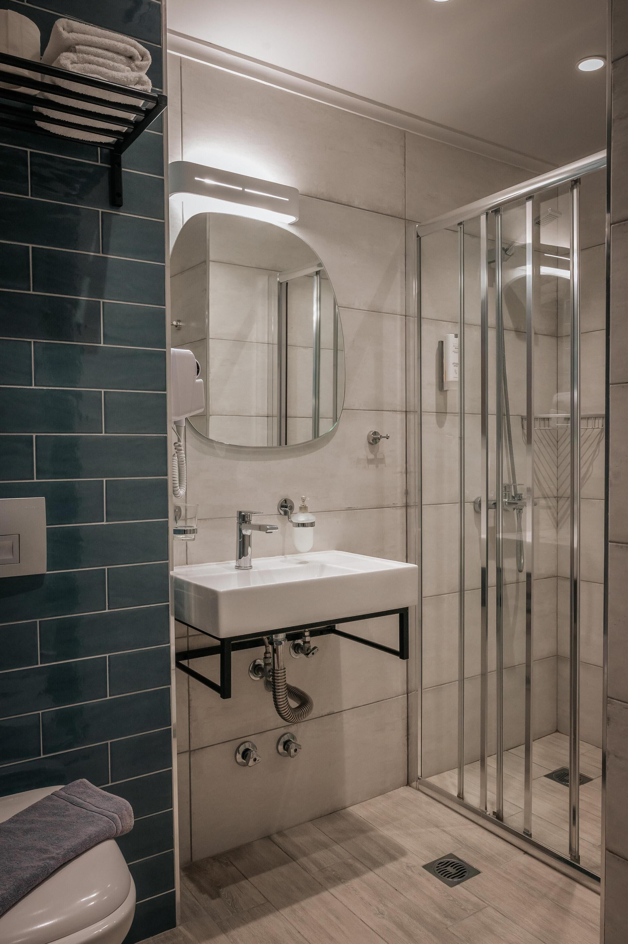 Une salle de bain moderne avec une douche à parois de verre, un lavabo blanc avec un miroir au-dessus, et un porte-serviettes avec des serviettes pliées.