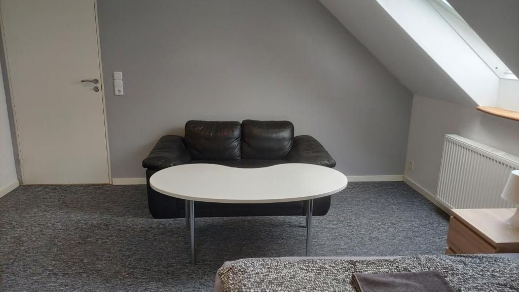 A room with a black leather sofa, a white table, and a grey carpet.
