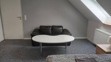 A room with a black leather sofa, a white table, and a grey carpet.