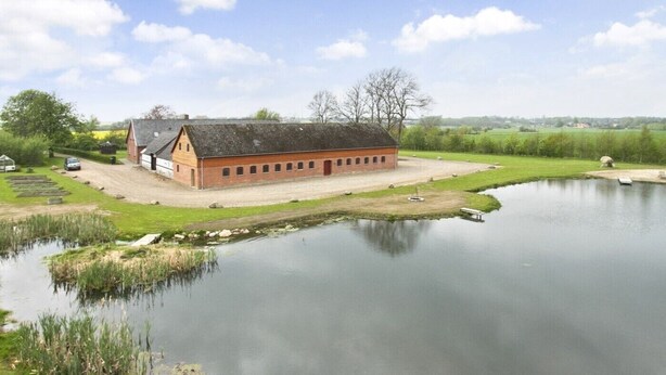 A large brick building with a sloped roof, surrounded by a pond and grassy areas. - Ringslund B&B (Galten)