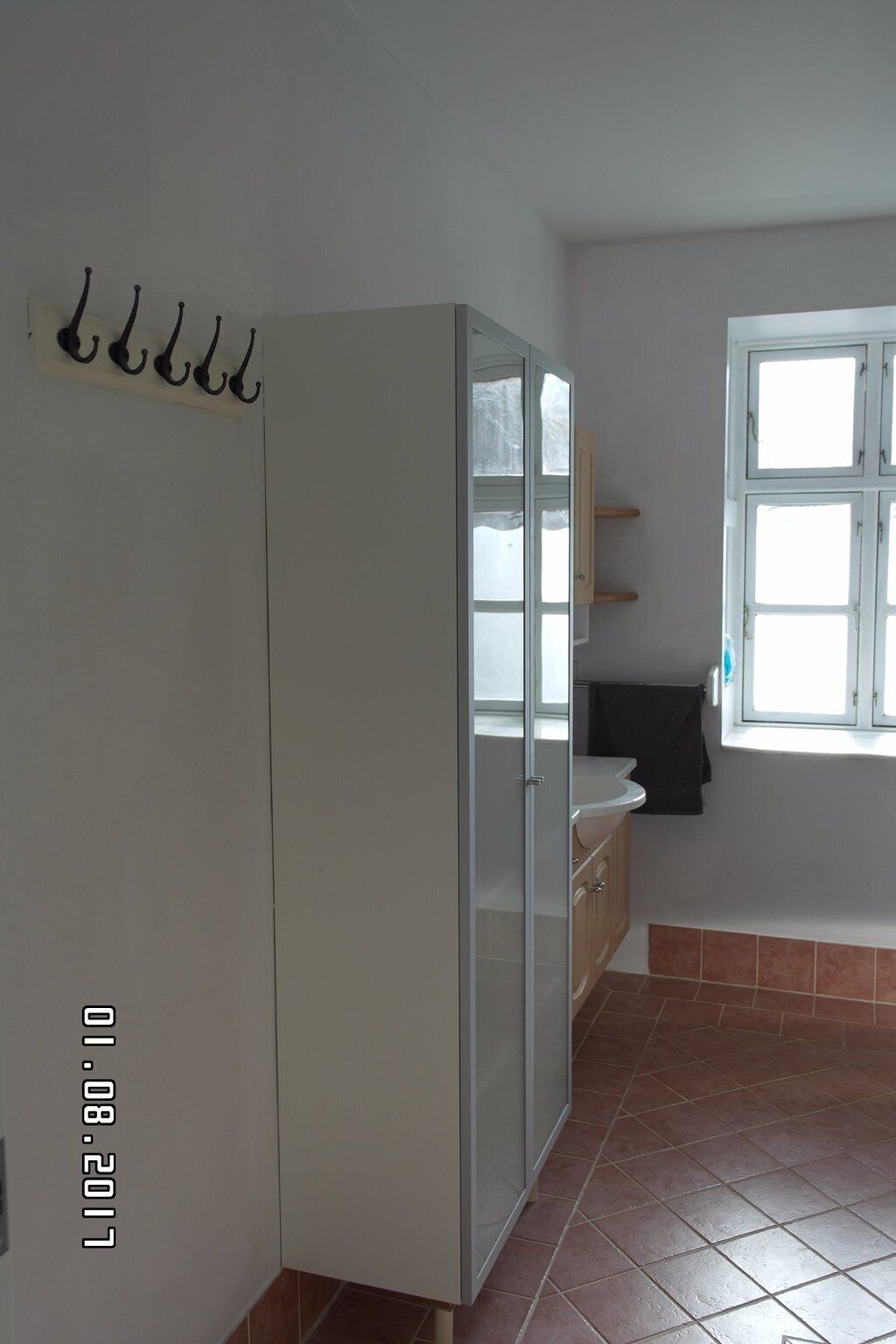 A room with a white wardrobe, a window with a view, and a tiled floor.