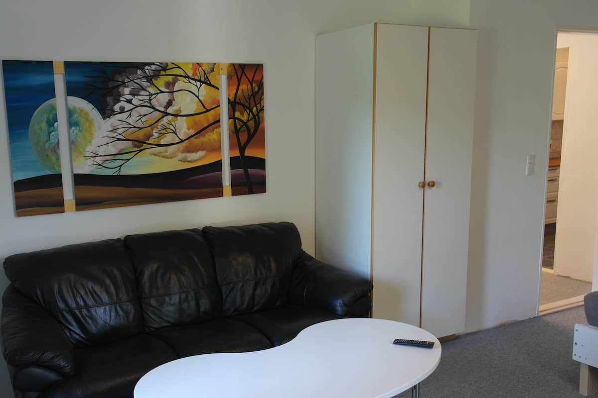 A living room with a black leather couch, a white coffee table, and a painting of a tree against a sunset.