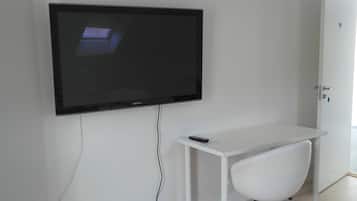 Un televisor de pantalla plana montado en una pared blanca, un escritorio blanco con un control remoto y una silla blanca.