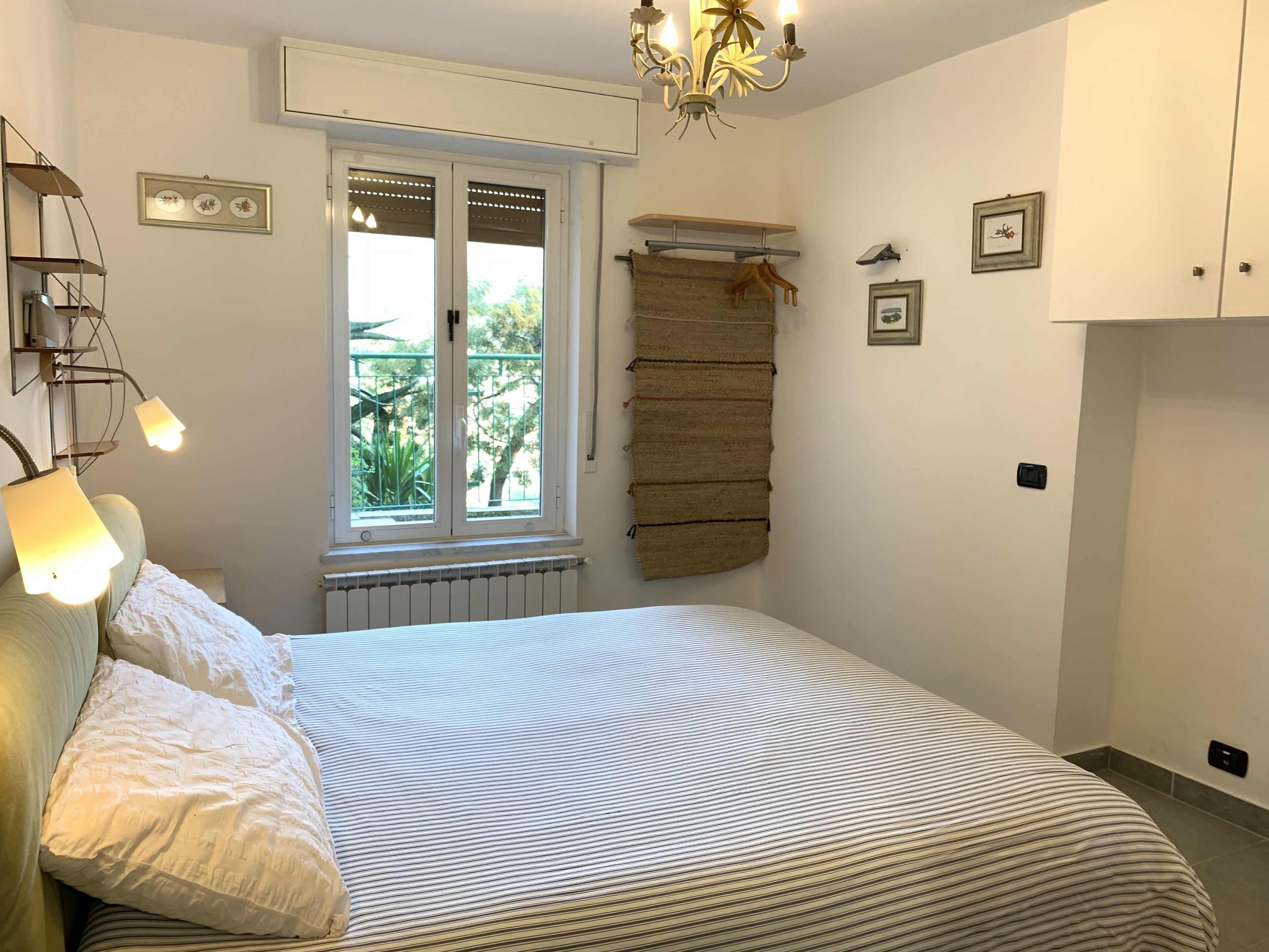 Ein Schlafzimmer mit Bett, Nachttischlampen, einem Fenster mit Ausblick, einer Heizung und Wandregalen.