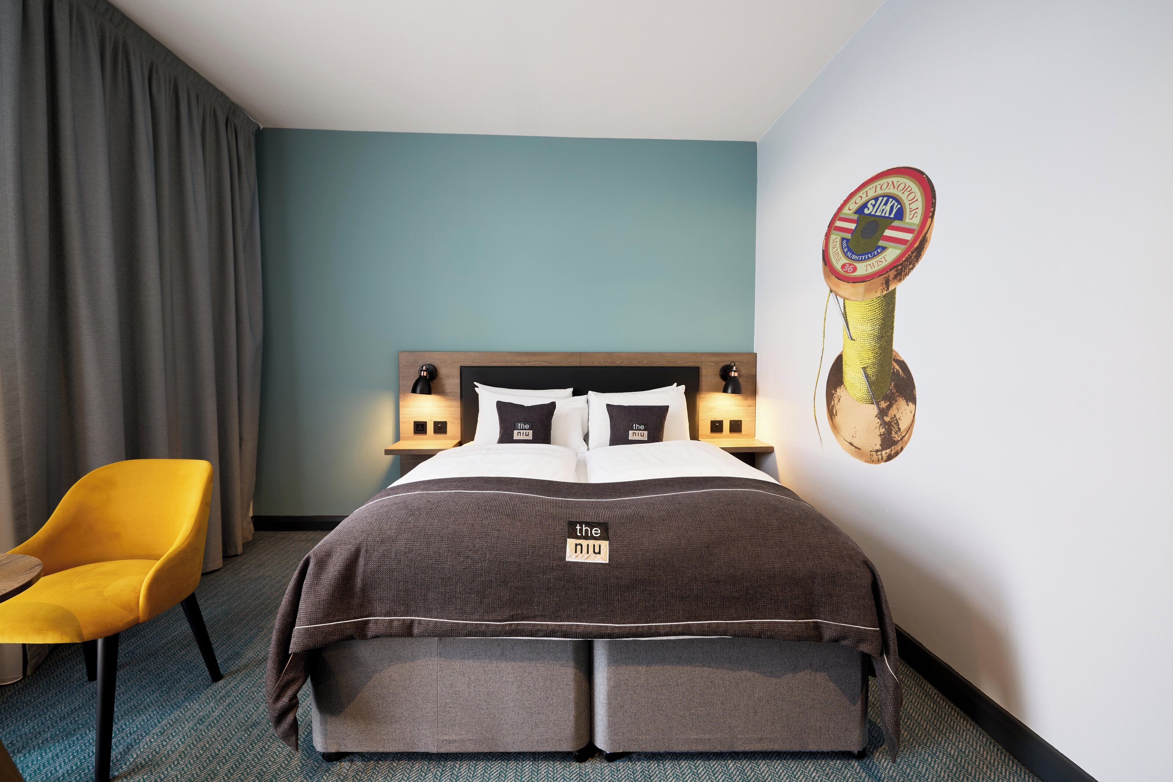 A hotel room with a bed, a yellow chair, and a wall-mounted cat toy.