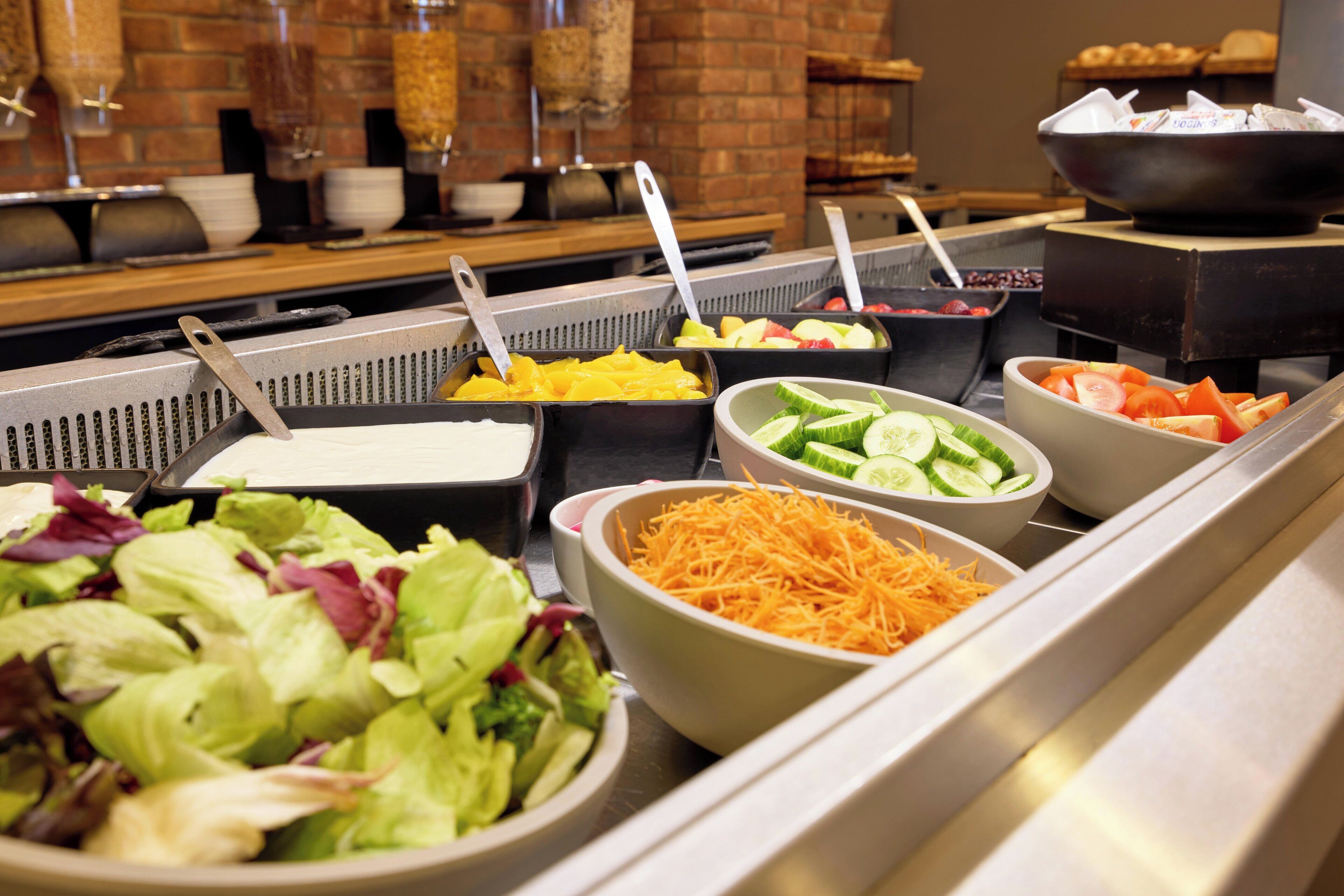 Un bufé con diversas opciones de comida, incluyendo ensaladas, frutas y queso rallado.