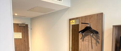 Ein Hotelzimmer mit einem Holznächtigstisch, einem Spiegel, einem Kleiderhaken und einer kleinen Ablage mit Bedienfeld.