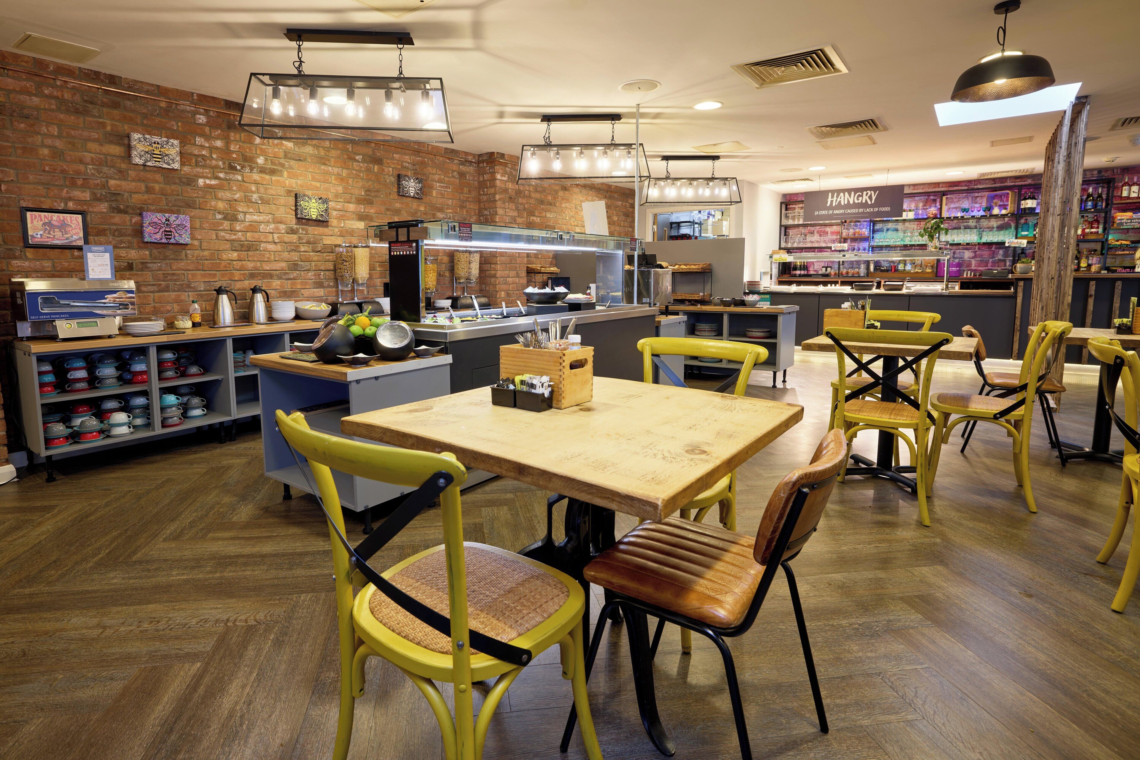 A restaurant interior with brick walls, wooden flooring, yellow chairs, and a bar area.