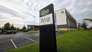 Un parking avec un panneau indiquant « the niu » et un bâtiment moderne en arrière-plan.