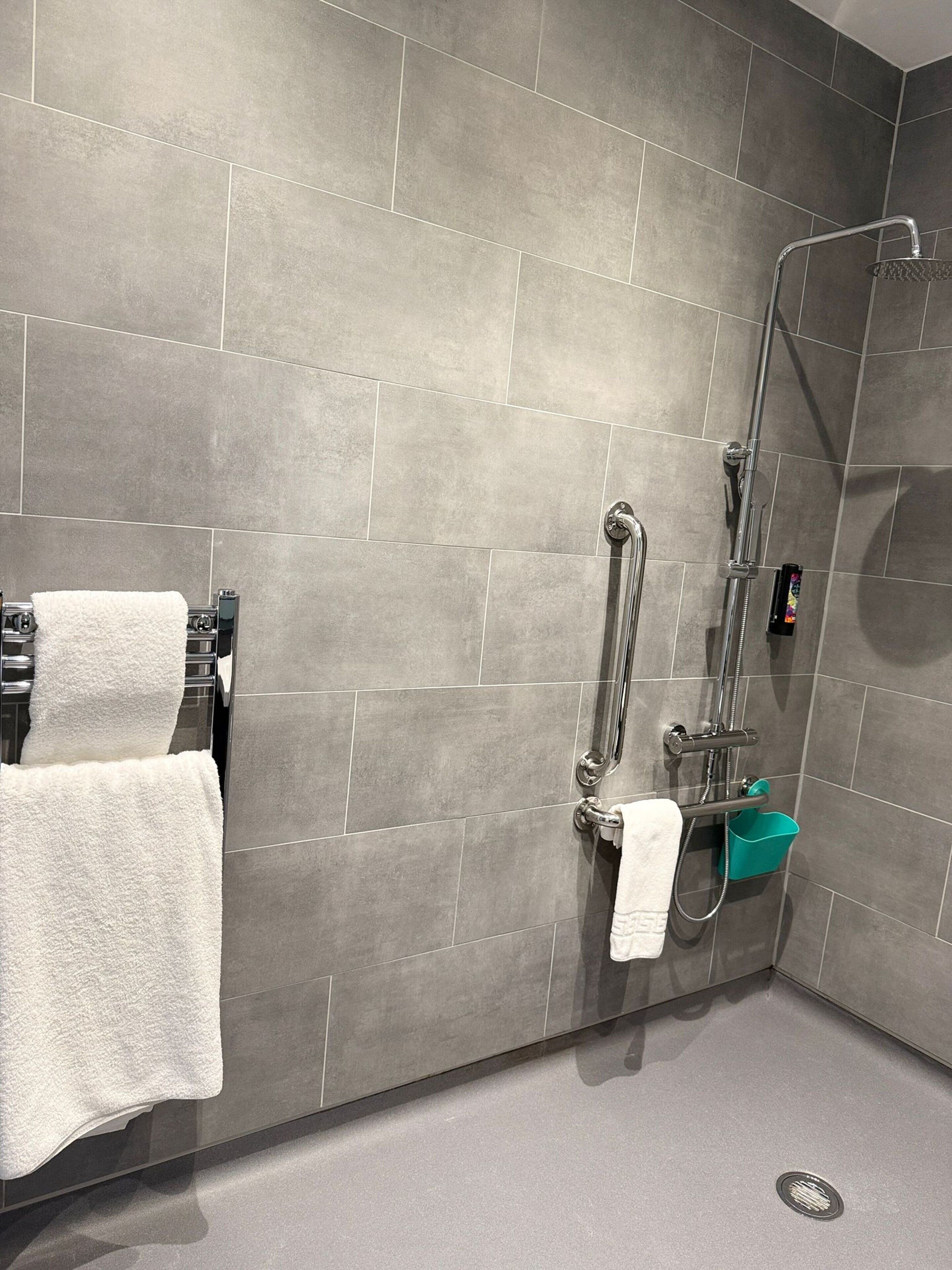 Un bagno moderno con piastrelle grigie, una doccia, una vasca da bagno e un porta asciugamani.