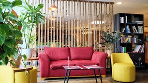 Un salon moderne avec un canapé rouge, un fauteuil jaune et une cloison en bois dotée de lattes verticales.