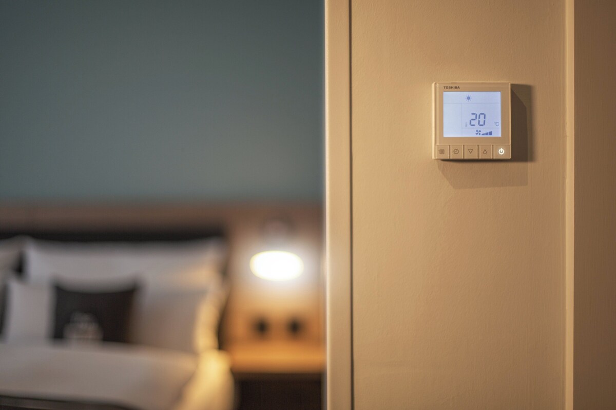 A thermostat on a wall displaying a temperature of 20°C.