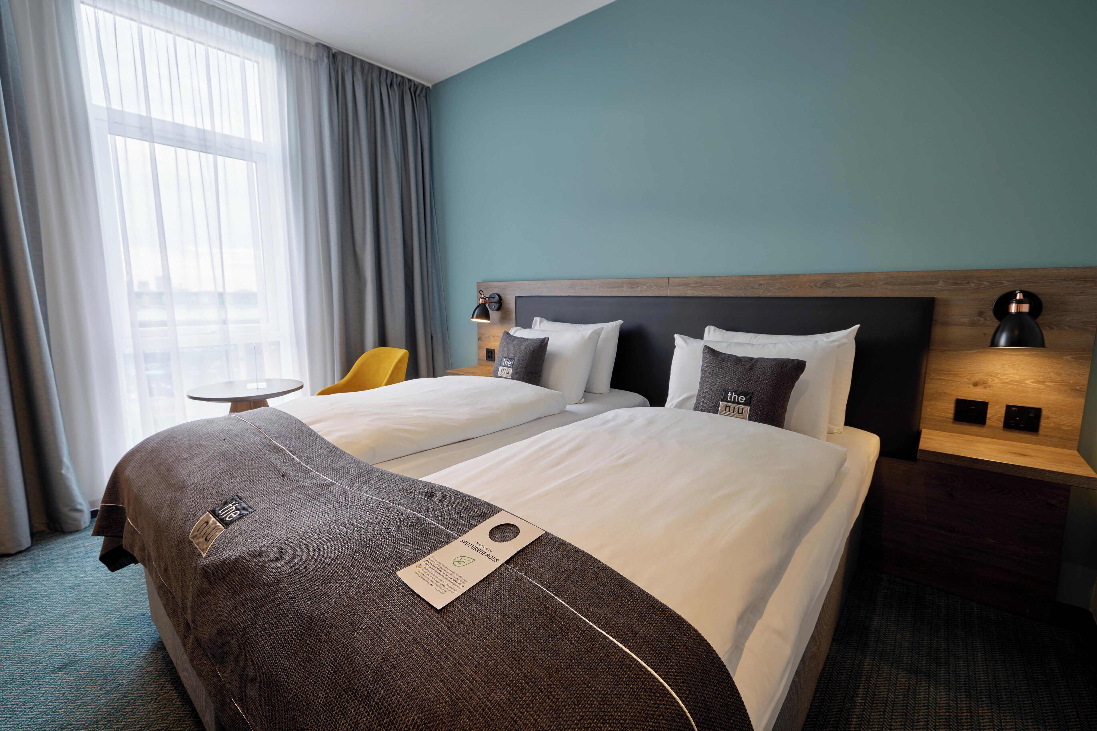 Een hotelkamer met twee bedden, een klein tafeltje, een stoel en een raam met gordijnen.