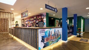 Un espace d’accueil d’hôtel avec un comptoir où sont exposés divers équipements, un panneau indiquant les directions et une fresque représentant un paysage urbain.