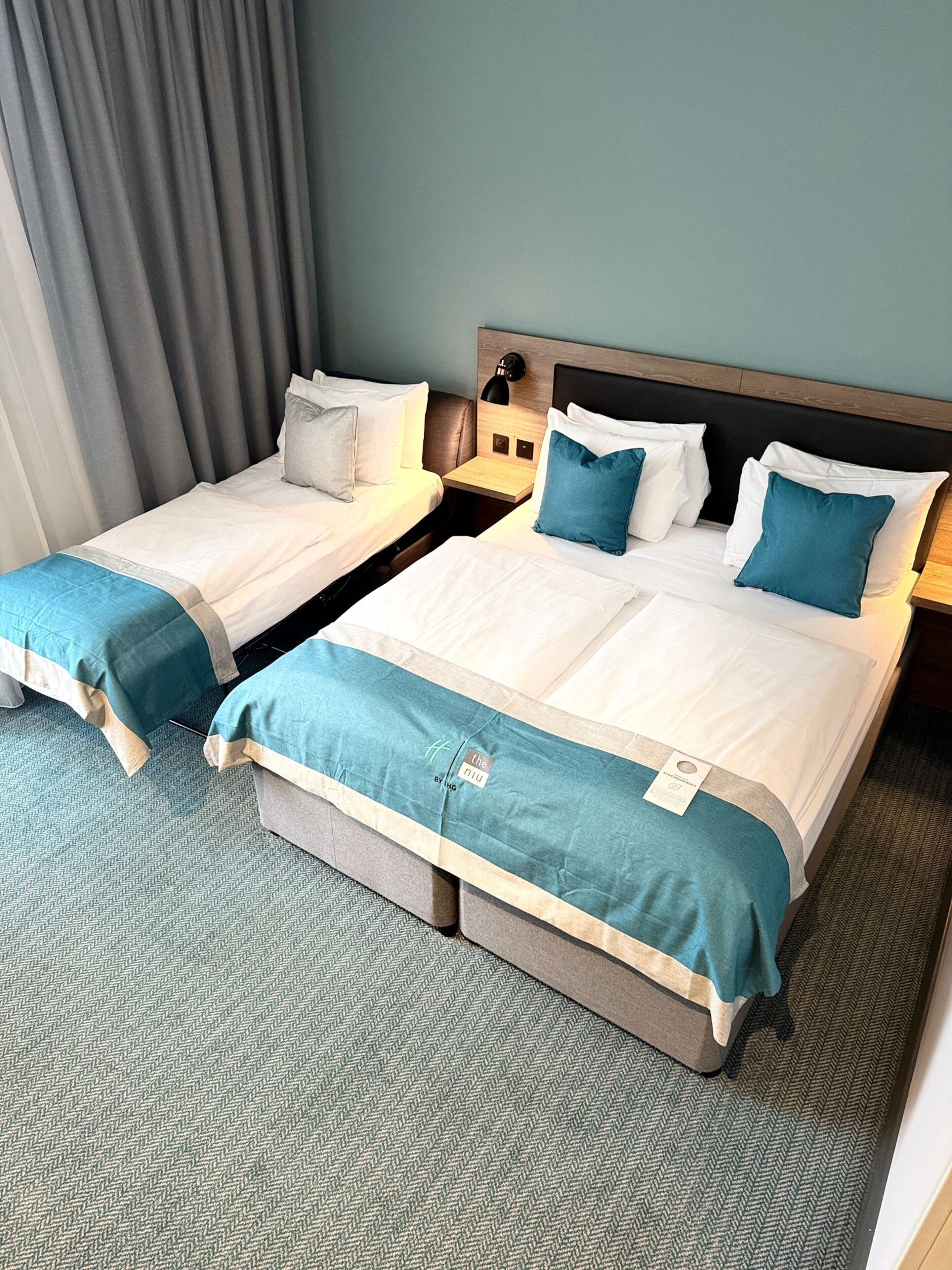 A hotel room with two beds, each with a blue and white bedspread, a wooden headboard, and a nightstand with a lamp.