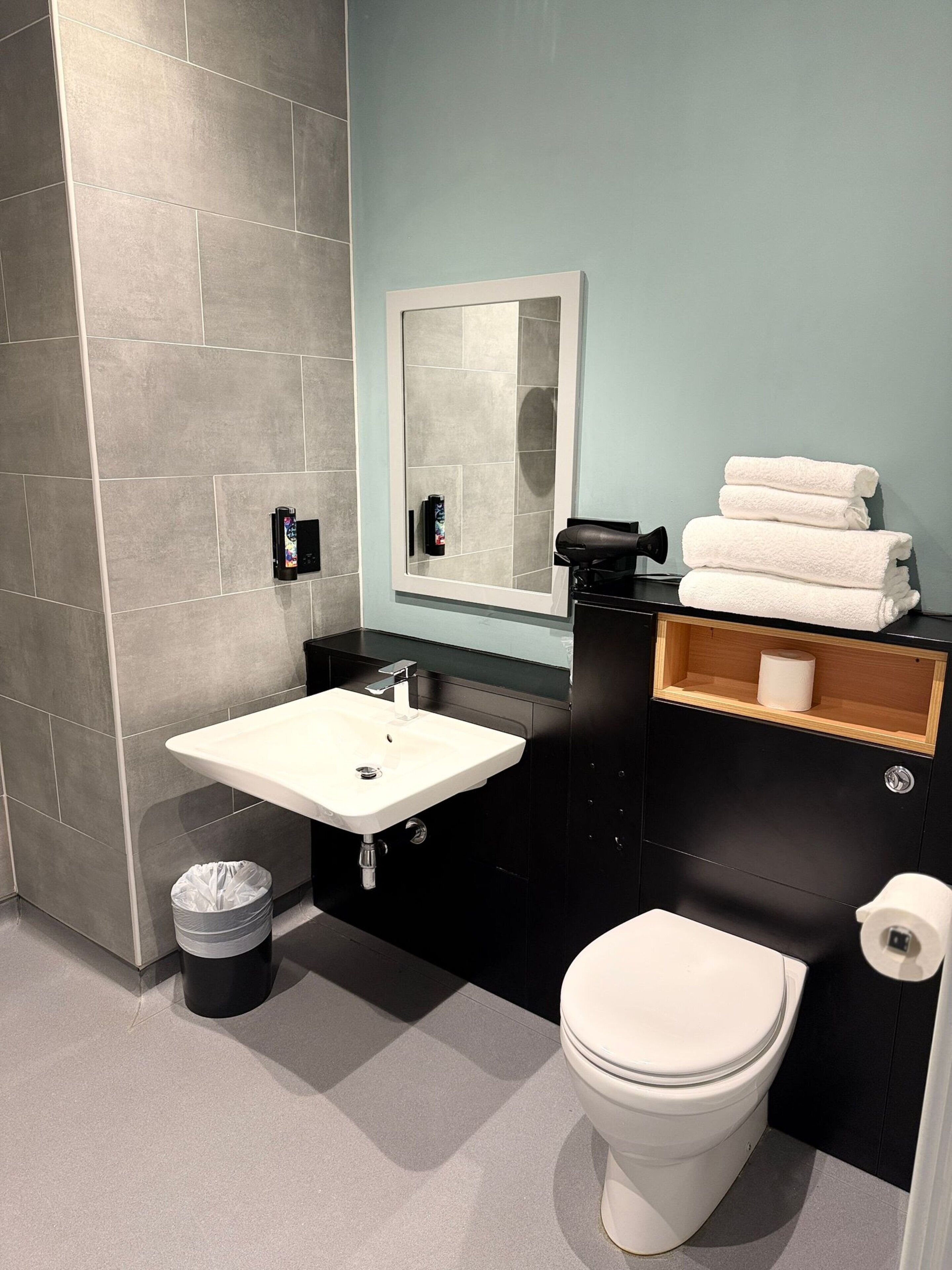 A modern bathroom with a white sink, black vanity, a mirror, and a toilet.