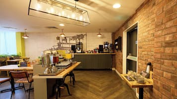 Un café acogedor con suelo de madera en espiga, pared de ladrillo y una isla central con una máquina de café y un dispensador grande de bebidas.