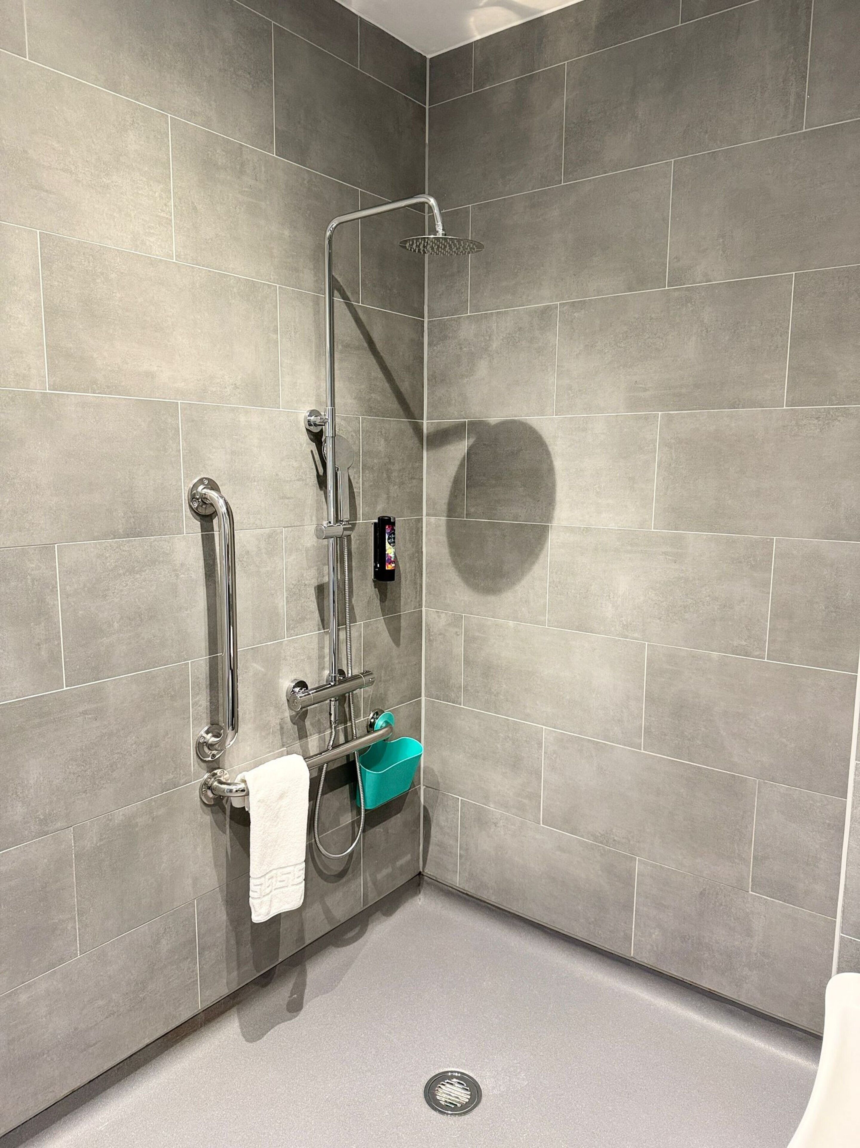 Un espace douche moderne avec des carreaux gris, une douchette à main et un support pour douchette, ainsi qu’un porte-serviettes.