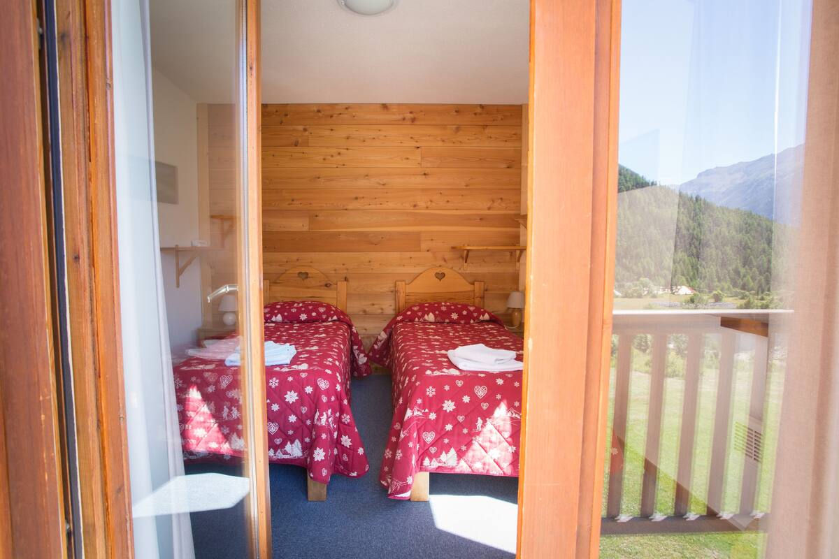 Habitación con dos camas, paredes de madera y un balcón con barandilla.