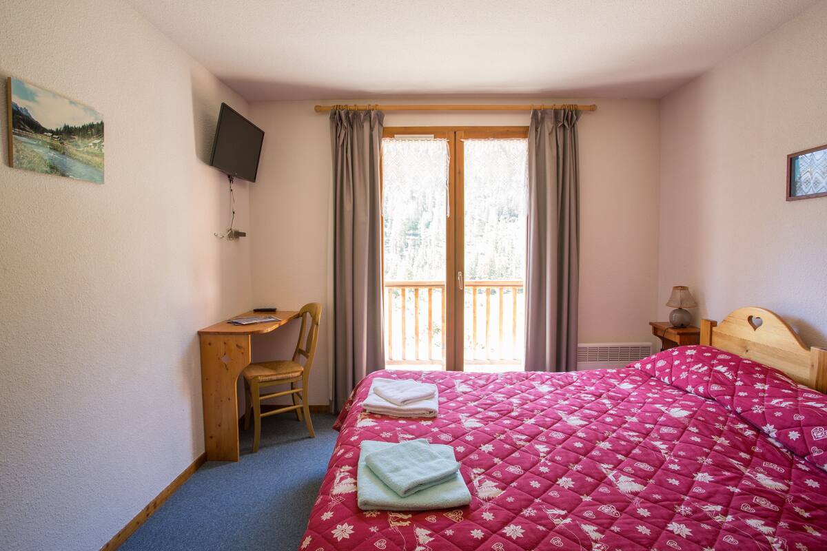 Un dormitorio con cama, escritorio, silla, televisión y ventana con cortinas.