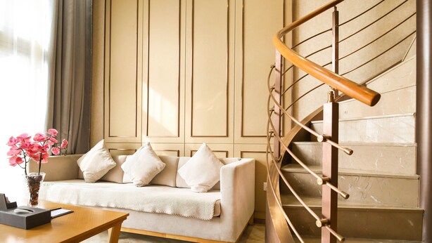 Una sala moderna con un sofá, una mesa de centro de madera y un florero con flores rosas. Se ve una escalera con barandilla de madera a la derecha.