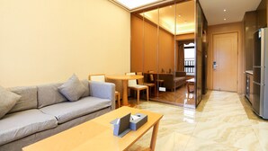 Una sala moderna con un sofá, una mesa de centro de madera y un separador de vidrio que da a un comedor con una mesa y sillas.